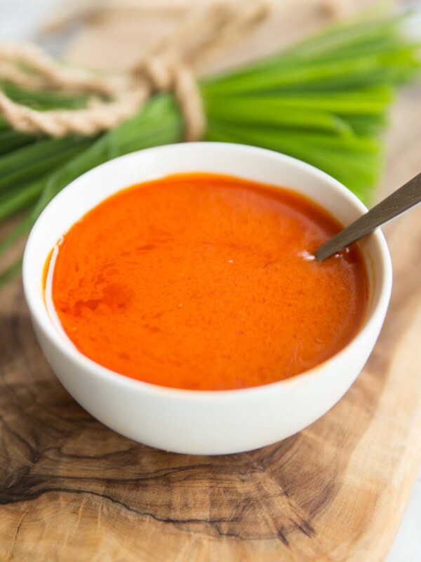 buffalo sauce in a small white pot with spoon in it and chives blurred in the background