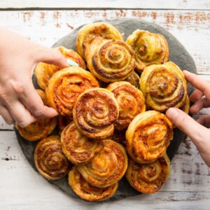 overhead shot of puff pastry pinwheels on slate with two hands grabbing a pinwheel