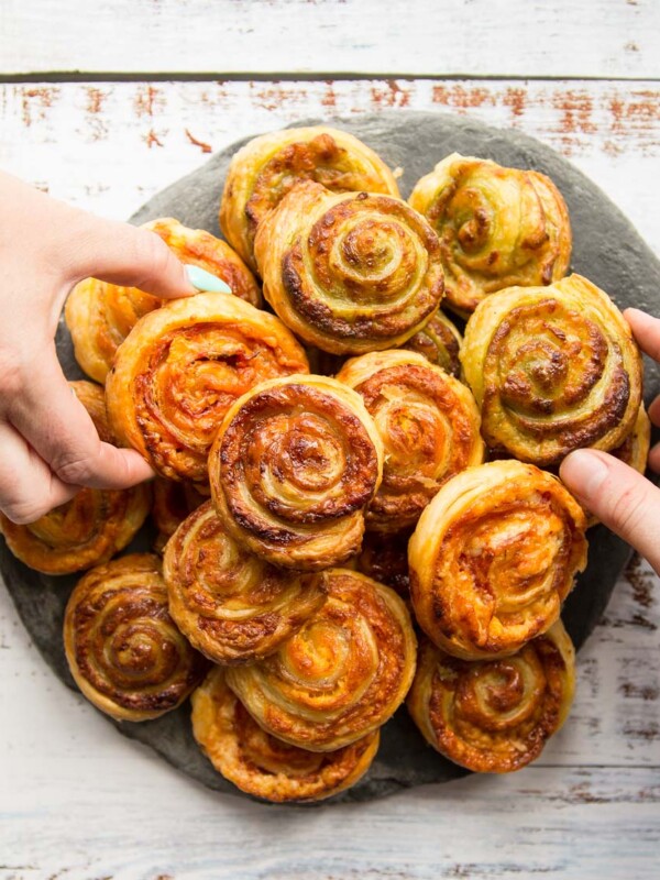 overhead shot of puff pastry pinwheels on slate with two hands grabbing a pinwheel