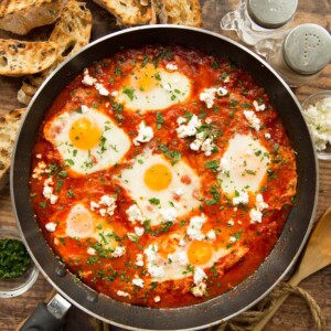 overhead shot of shakshuka in pan surrounded by ciabatta and seasonings