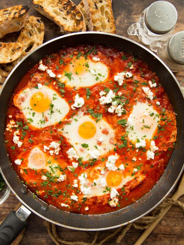 overhead shot of shakshuka in pan surrounded by ciabatta and seasonings