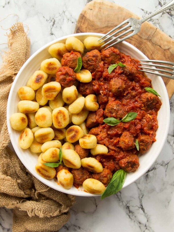 overhead shot of gnocchi and sausage meatballs in white bowl on brown chopping board