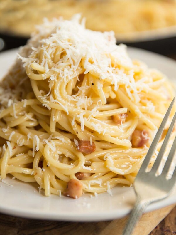 spaghetti carbonara on white plate with saucepan blurred in background and fork resting on plate