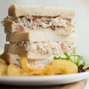 3 half sandwiches stacked on a white plate with crisps and salad leaves