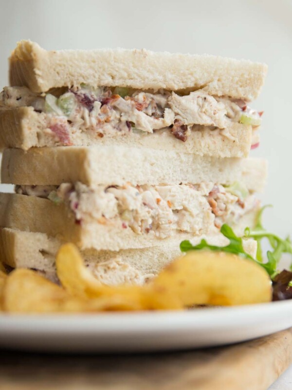 3 half sandwiches stacked on a white plate with crisps and salad leaves