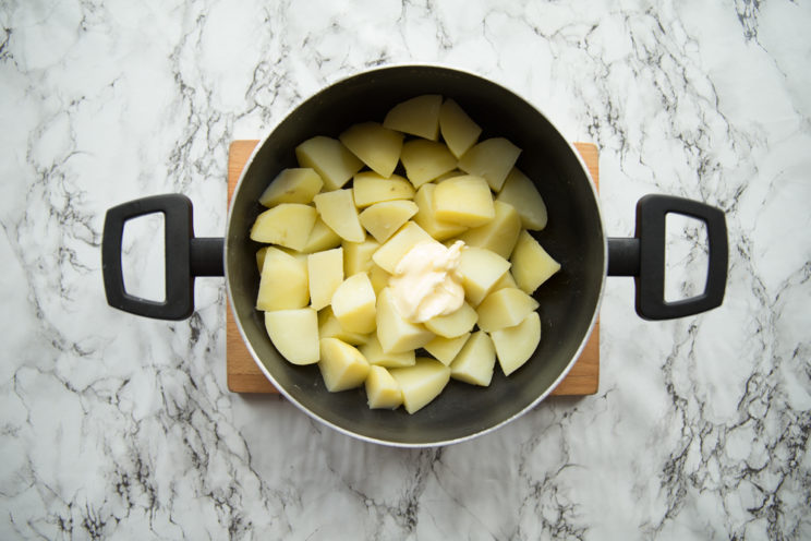 boiled potatoes with butter in black pop on chopping board