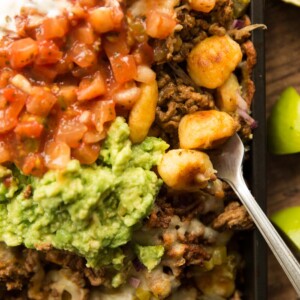 overhead shot of gnocchi nachos in tray with guac, salsa ad sour cream