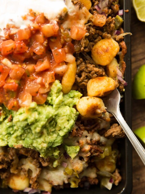 overhead shot of gnocchi nachos in tray with guac, salsa ad sour cream