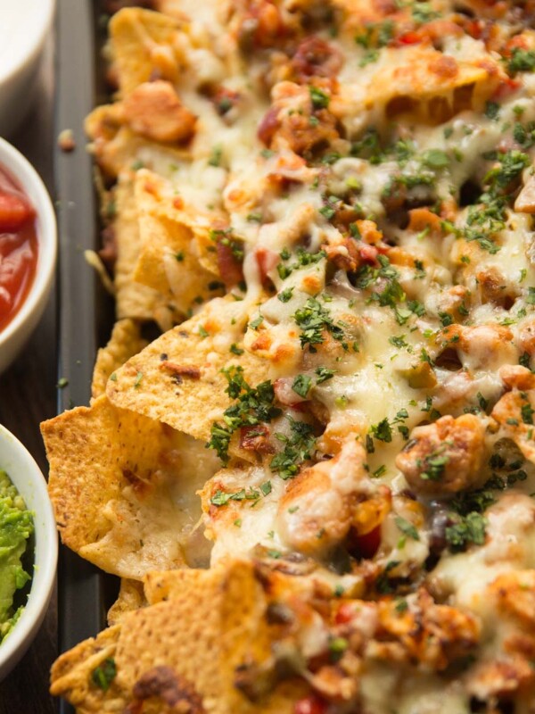 chicken fajita nachos garnished with coriander served on a tray with dips next to them