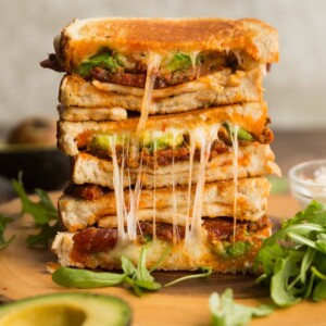 halloumi grilled cheese sandwich stacked on wooden board surrounded by rocket