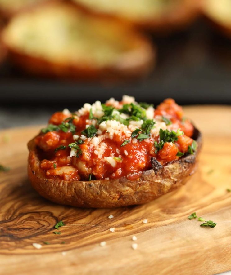 close up shot of bolognese in potato skin on chopping board garnished with parsley and parmesan