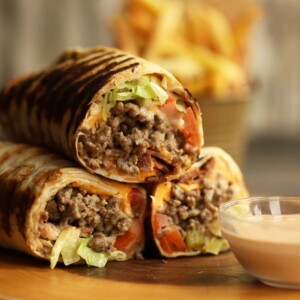 cheeseburger wraps stacked on top of each other on wooden board with fries blurred in background