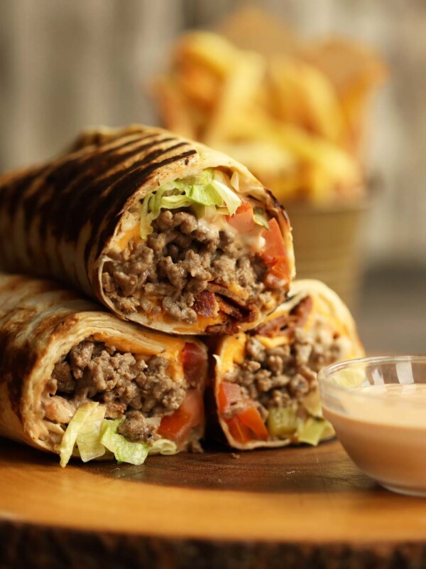 cheeseburger wraps stacked on top of each other on wooden board with fries blurred in background