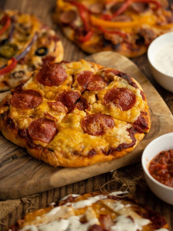 4 different pizzas, focus on one sat on wooden chopping board