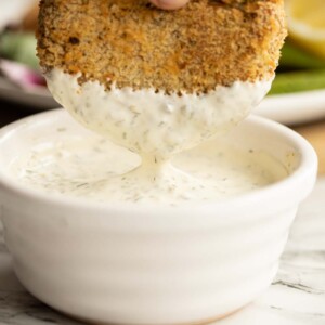 dunking tuna fish cakes into small white pot of tartare sauce