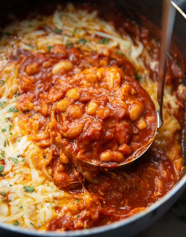 ladle scooping out cheesy beans in large pot