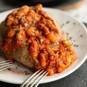 beans poured on baked potato on white plate with two silver forks resting