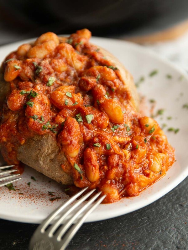 beans poured on baked potato on white plate with two silver forks resting