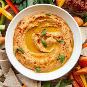 overhead shot of white bowl of hummus surrounded by veg and pita chips