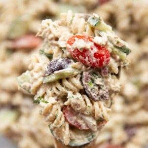 pasta salad resting on salad spoon held above bowl of salad