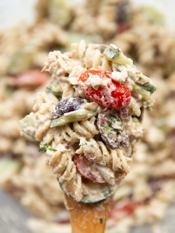 pasta salad resting on salad spoon held above bowl of salad