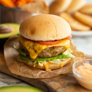 burger in wooden chopping board with buns and sweet potato fries blurred in background