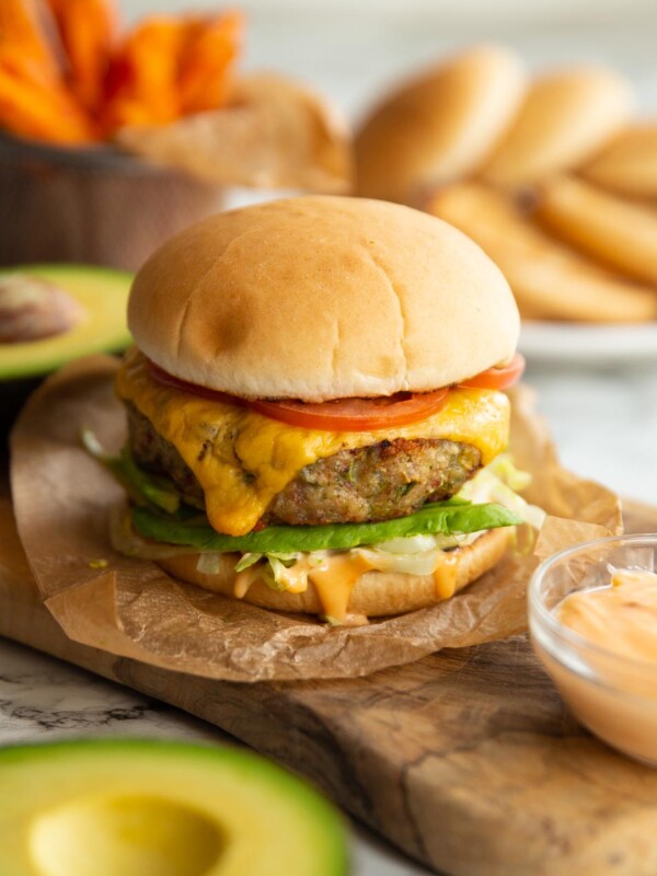 burger in wooden chopping board with buns and sweet potato fries blurred in background