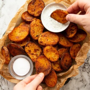 overhead shot of potatoes un scrunched paper with pot of dip and salt with hands reaching in