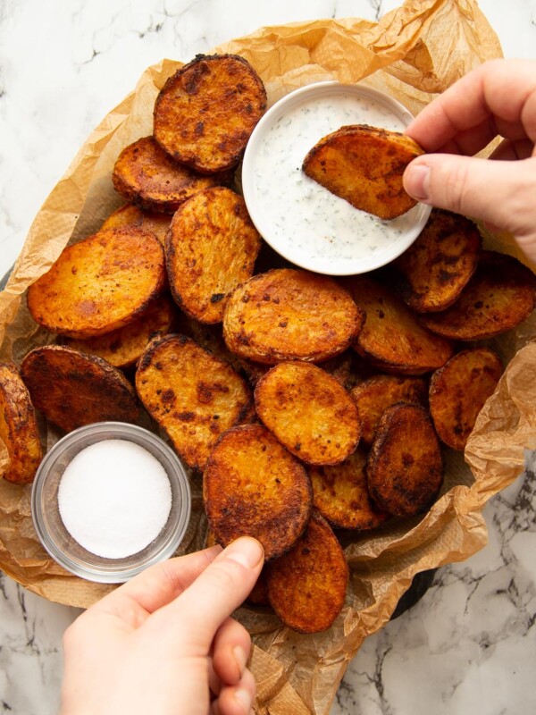 overhead shot of potatoes un scrunched paper with pot of dip and salt with hands reaching in