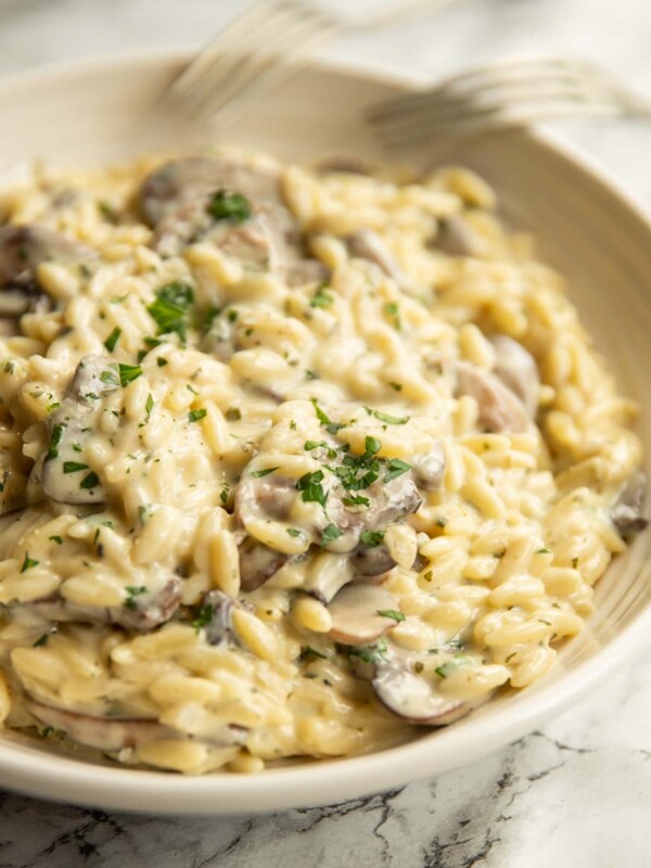 orzo in white bowl garnished with parsley with two forks resting on bowl