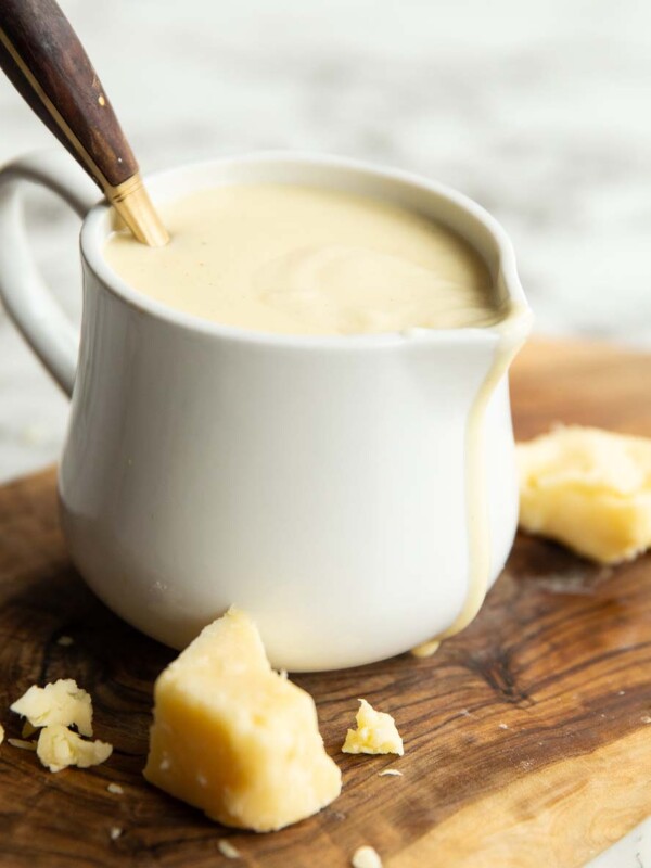 cheese sauce in small white jug with gold spoon digging in