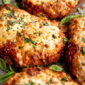 close up shot of chicken parmas fresh out the oven garnished with basil