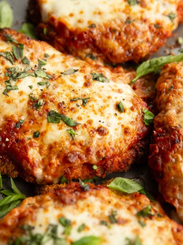 close up shot of chicken parmas fresh out the oven garnished with basil