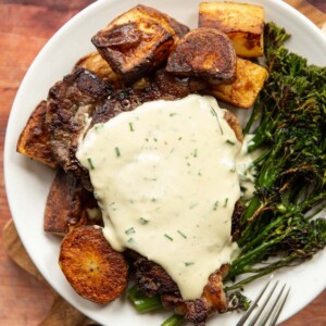 overhead shot of steak with sauce served with potatoes and broccolini on white plate