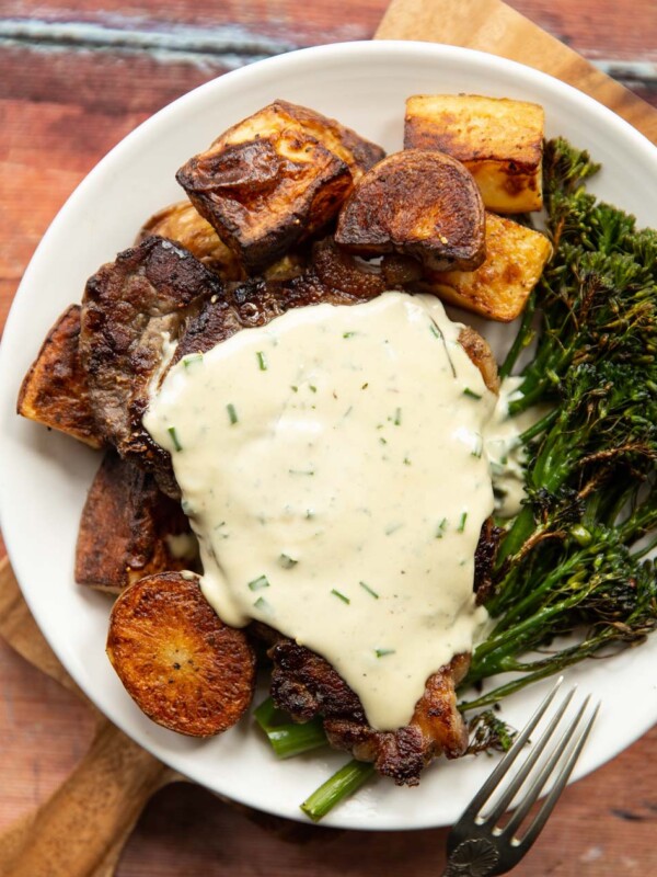 overhead shot of steak with sauce served with potatoes and broccolini on white plate