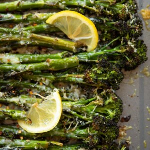 overhead shot of broccolini on grey oven tray with lemon wedges