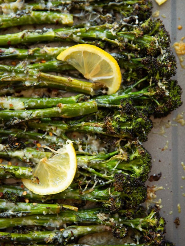 overhead shot of broccolini on grey oven tray with lemon wedges