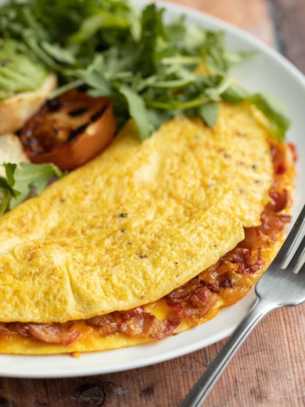 closeup shot of omelette on white plate with silver fork resting on it with salad blurred in background