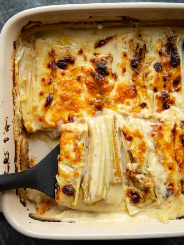 overhead shot of black plastic spatula digging into cheesy leeks in baking dish