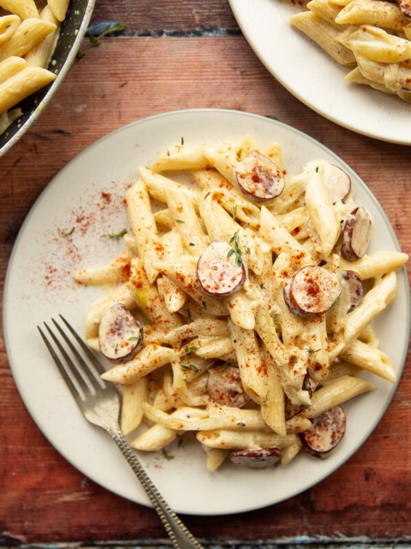 overhead shot of pasta on white plate with silver fork on wooden background