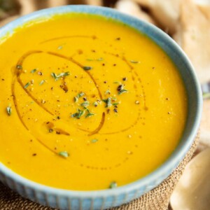 carrot soup in small blue bowl wrapped in brown cloth