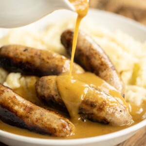 pouring gravy over sausages on mashed potato in white bow