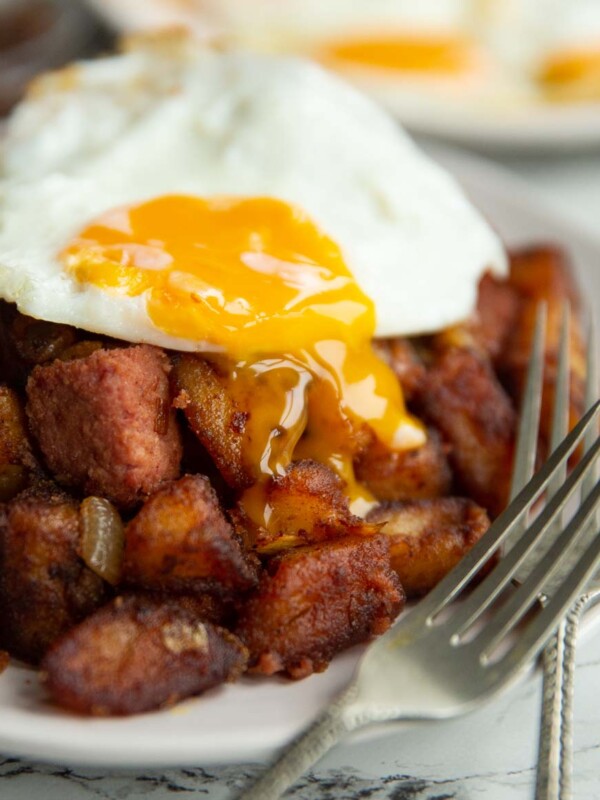 fried egg on corned beef hash with yolk dripping down on white plate