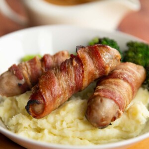 sausages on bed of mashed potato with jug of gravy blurred in background