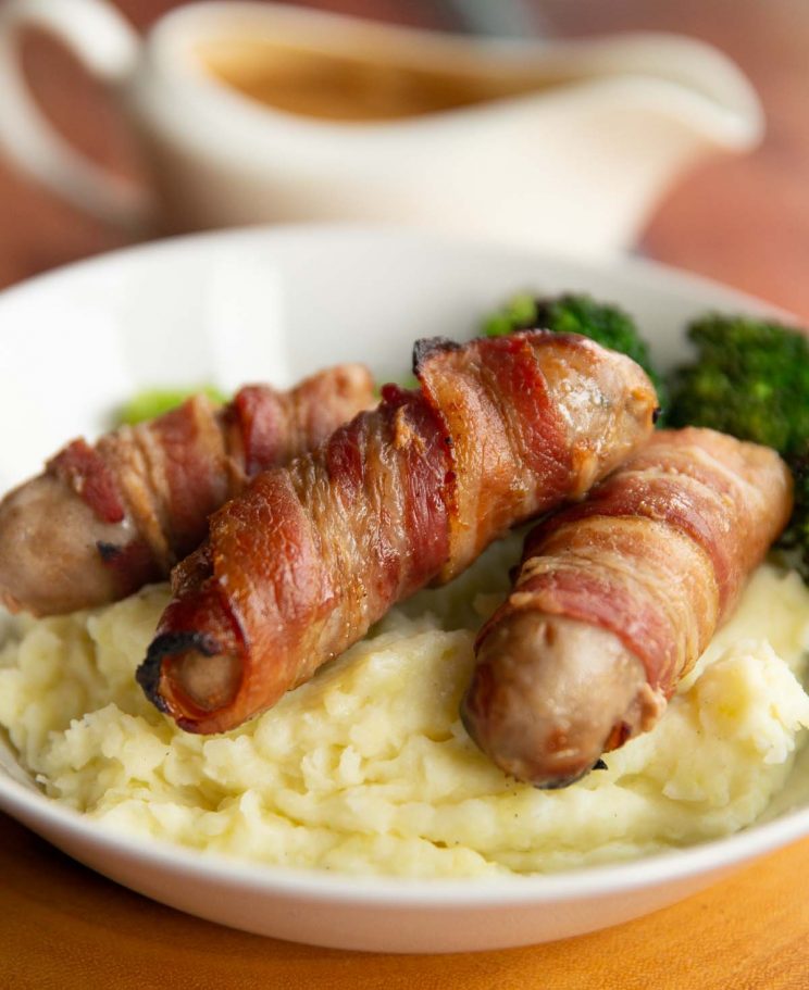 sausages on bed of mashed potato with jug of gravy blurred in background