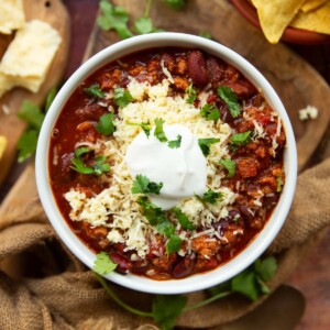 overhead shot of chili in white bowl with sour cream, cheese and cilantro