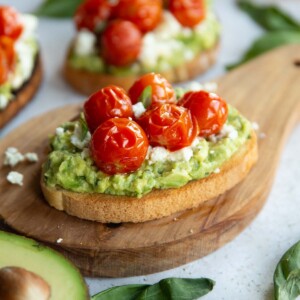 tomato avocado toast on wooden board surrounded by toast and garnish