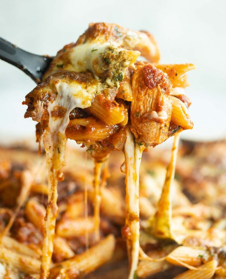 serving spoon scooping out pasta from dish with cheese pull