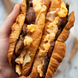 overhead shot of hand holding two croissants above chopping board