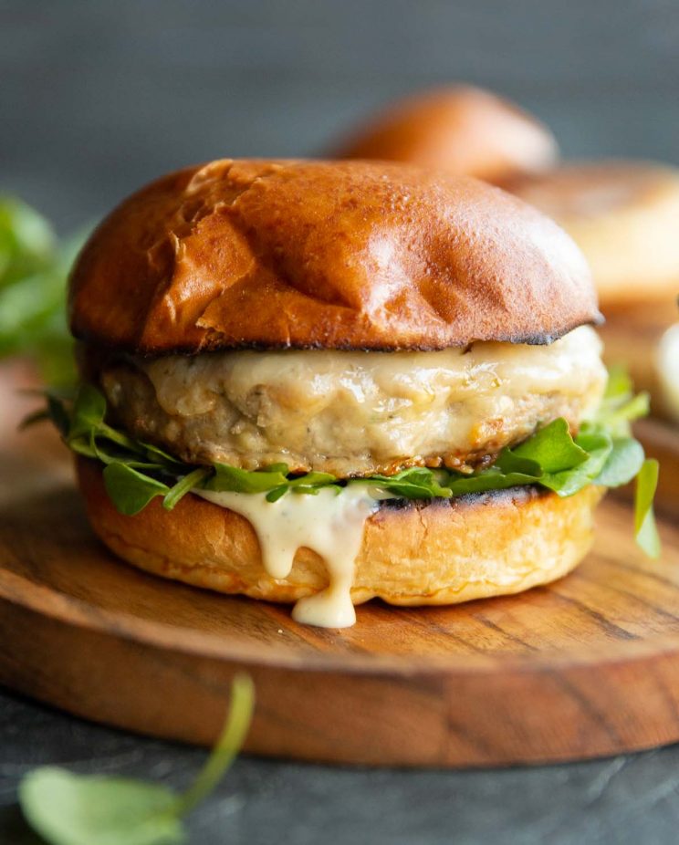burger on small wooden board with buns and watercress blurred in background
